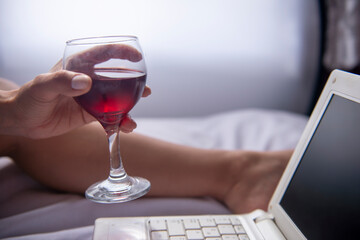 businesswoman drinking wine while working on notebook computer in bedroom
