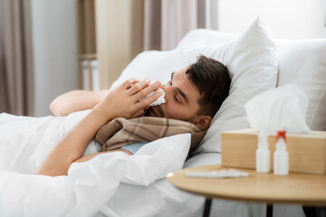 people and health problem concept - unhappy sick man blowing nose lying in bed at home