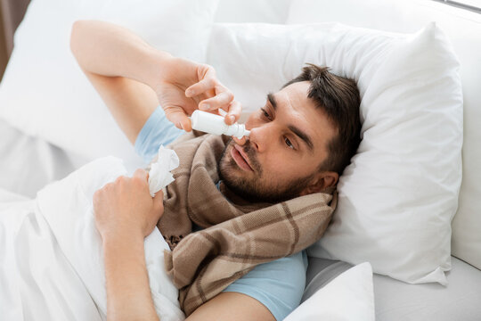 people and health problem concept - unhappy sick man spraying his nose with nasal spray lying in bed at home