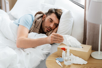 people and health problem concept - unhappy sick man lying in bed at home and taking paper tissue from box