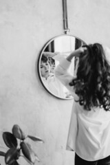 a woman in a white shirt looks at reflection in a round mirror. black and white 