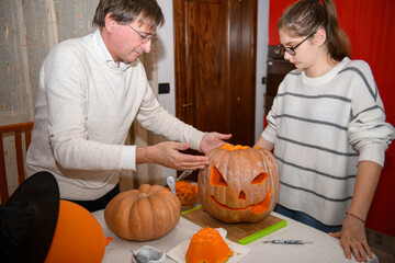 Father and daughter carving pumpkin, Jack o lanterns on Halloween at the kitchen. Celebrating Halloween at home with a Creepy Pumpking, Decoration for fall party. Traditional autumn holiday