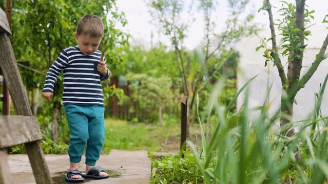 little blond boy with a wooden sword in his hands jumps into a puddle