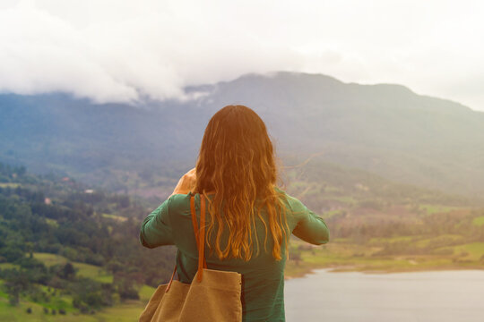 Woman from the back taking a photo with her cell phone of a landscape of a lake with mountains