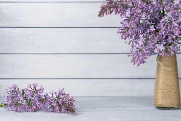 Bouquet of lilac flowers in vase and branch on table on grey wooden background. Copy space