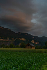 House at dusk after sunset in Dornbirn, Vorarlberg, Austria. pink and grey-blue clouds over the green meadows, trees, barns and mountains. Interesting and impressive cloud mood