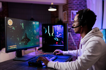 Young gamer playing online shooting video games, streaming action rpg competition on pc with neon lights. Male streamer having fun with esport gaming championship on computer.