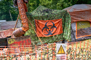 Tent with a camouflage net and a loge with the warning of a biohazard in a tent camp after the...