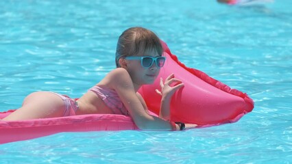 Young child girl relaxing on summer sun swimming on inflatable air mattress in swimming pool during tropical vacations. Summertime activities concept