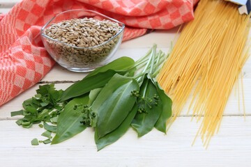 Wild garlic, lat. Allium ursinum, on cutting board.  Leaves of fresh ramson, sunflower seeds and raw spaghetti.