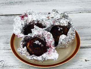 Baked red beet removed from the oven.  Red beetroot baked in aluminum foil on the plate.