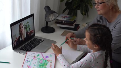 Fototapeta na wymiar little girl studying with her grandmother at home, use laptop for education, online study, home studying. Girl has homework at distance learning. Lifestyle concept for Family quarantine covid-19.