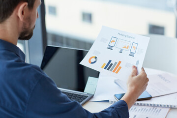 Close up of business person holding document with data and statistics charts while working at desk, copy space