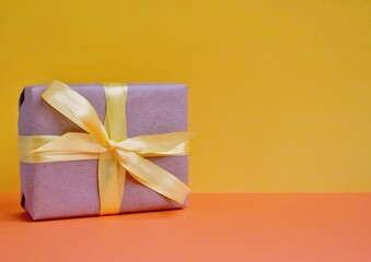 A wrapped gift with a yellow bow in the middle on an orange-yellow background. Festive background. Holiday gift. Bright postcard. Place for text.