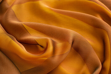Background from silk fabric of yellow brown color. Sheer fabric creates a textured background. Textile in the form of silk.