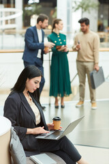 Vertical portrait of Middle Eastern businesswoman using laptop while sitting in waiting area of modern office building