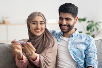 Joyful Muslim Spouses Holding Positive Pregnancy Test Celebrating Result Indoors