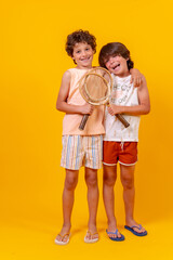 Portrait of two brothers playing tennis on summer vacation, yellow background