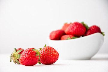 Close-up of three strawberries on a white table with a bowl in the background, selective focus, white background, horizontal, with copy space