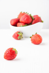 Strawberry closeup on white table with bowl in the background, selective focus, white background, vertical, with copy space