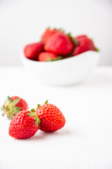 Close-up of three strawberries on a white table and white background, with a bowl in the background, selective focus, vertical, with copy space