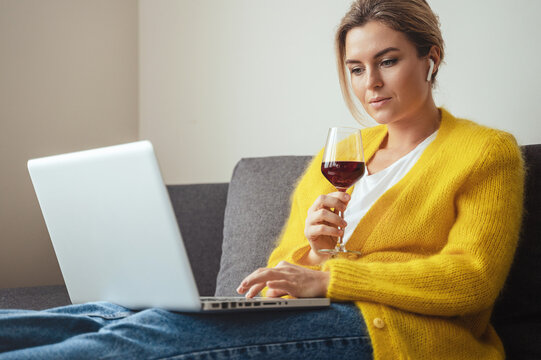 Woman sitting on the sofa drinking red whine while watching movie or working on her laptop at home
