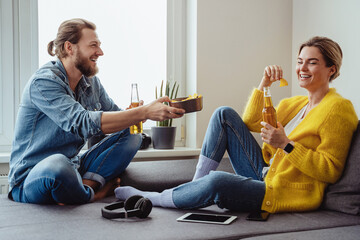 Young cheerful couple sitting on the sofa drinking beer and eating nachos