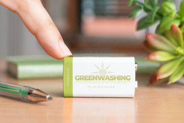 Greenwashing concept, woman hold a finger over a battery with the text: greenwashing, we care about the planet