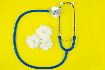 Blue phonendoscope lies on a bright yellow background with white flowers inside. High quality photo