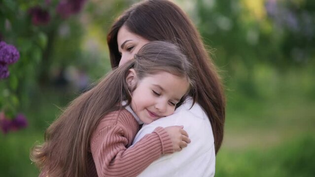 A young mother holds a cute little daughter in her arms near a flowering tree. Portrait of a four-year-old girl in the arms of a loving mother.