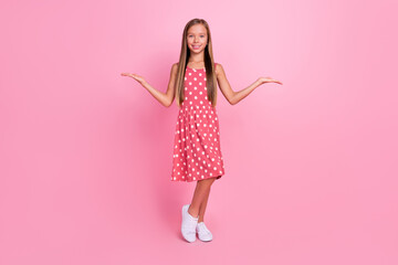 Full length portrait of little schoolgirl arms palms demonstrate empty space scales isolated on pink color background
