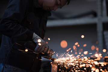 Heavy Industry Engineering Factory Interior with Industrial Worker Using Angle Grinder and Cutting a Metal Tube. Contractor in Safety Uniform and Hard Hat Manufacturing Metal Structures.
