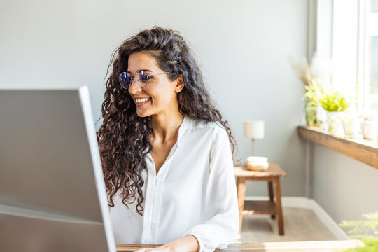 Portrait of young smiling woman looking at PC computer. Happy girl seating in creative office. Successful businesswoman. Modern business woman.