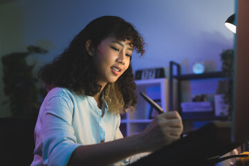 Young female designer working on the table in home studio and hand using digital pen on monitor screen with editor retouching photos.