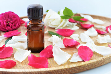 Essential oil of rose in a bottle and fresh flowers on a wooden table Natural cosmetics and aromatherapy