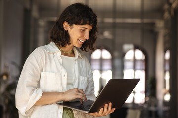Pretty young caucasian woman watches online webinar or training course on laptop indoors. Brunette...