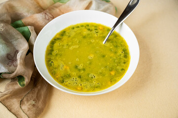 Pea and maize soup in white plate, spoon and scarf on yellow.