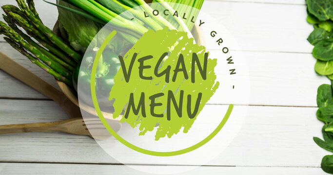 Image of locally grown vegan menu text in green, over bowl of fresh vegetables on white boards - Powered by Adobe