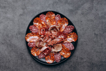 Different types of salami on a black platter, an appetizer for white wine or Prosecco in a restaurant aperitif meal