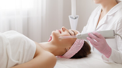 Young woman receiving darsonval procedure electric massage at beauty salon. Hardware cosmetology.