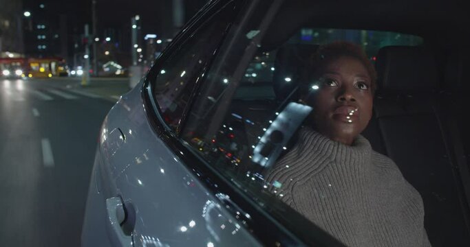 Hopefull young black woman is traveling by taxi in the night through downtown