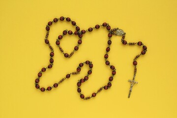 Rosary wooden beads and crucifix christian cross on yellow background. Catholic symbol. Flatlay, top view, lay out, isolated. Pray for God, faith in Jesus Christ and believe religion concept. Closeup