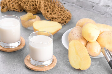 Vegan potato milk in two glasses and potato tubers on grey stone table background. Plant based alternative milk replacer and lactose free, Trendy healthy vegetarian and vegan drink concept