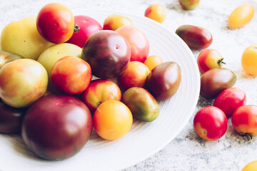 Various colorful tomatoes on white plate on stone table