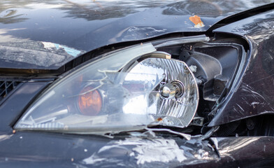 Broken headlights as a result of a collision. Broken black car after an accident. Car accident concept. Damaged emergency headlight, hood and bumper. Damage to the car body after the accident.