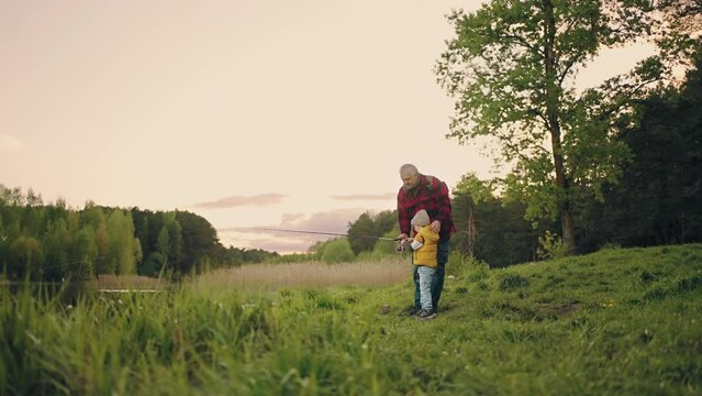 grandpa and grandson are fishing together in lakeshore, beautiful landscape in summer or spring day