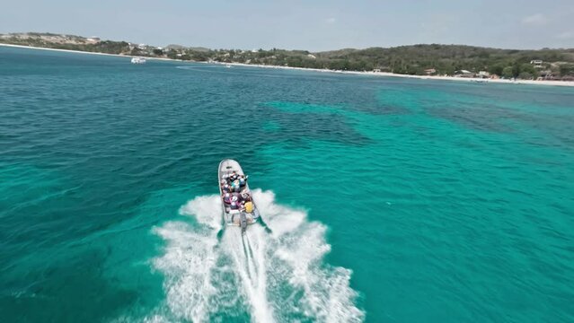 Acrobatic drone flying over tourist boat navigating in blue sea along Playa Ensenada beach in Dominican Republic. Aerial fpv