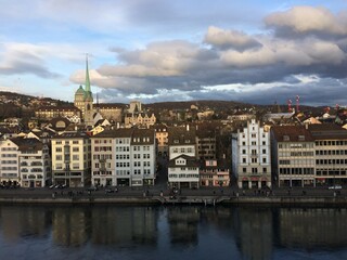 View from the highest point of the old town in Zürich over the Limmat River until the Zürichberg. Buildings are reflected in the water and the ETH and Polyterrase also appear.