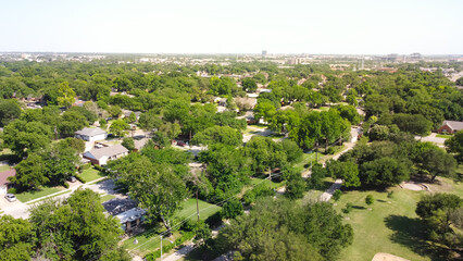 Aerial view typical residential neighborhood surrounded by park and lush green trees with downtown buildings in background in Richardson, Texas, USA