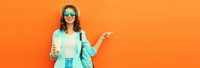 Summer portrait of happy smiling young woman with cup of coffee pointing finger to the side at blank copy space for advertising text on orange background